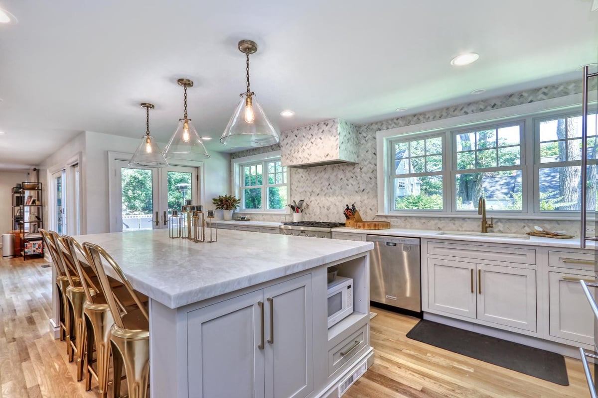Bright white kitchen remodel in Melrose, MA by PEGASUS Design-to-Build featuring a large island, marble countertops, and brass pendant lighting.-optimized