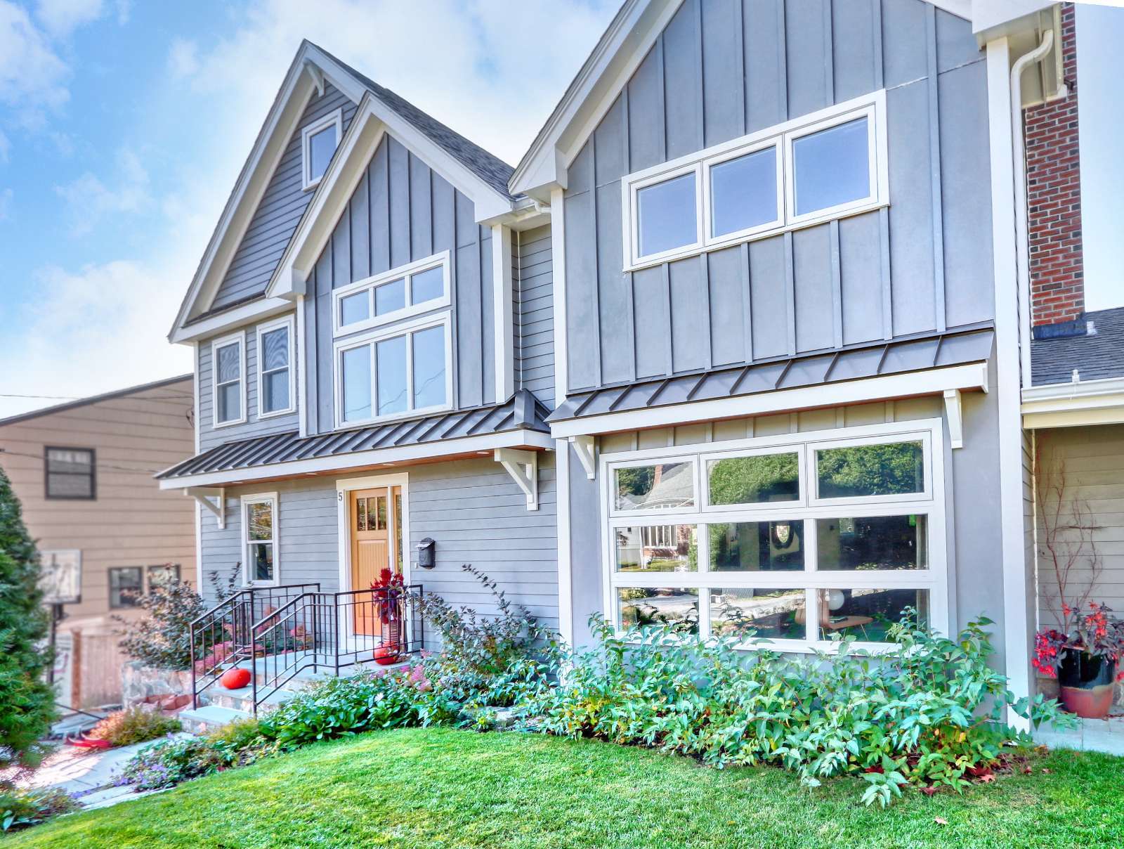 Front exterior home addition in Arlington, MA by Pegasus Design-to-Build with gray siding, large windows, and entryway landscaping-optimized
