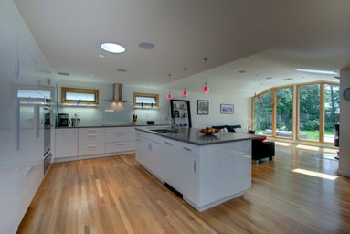 Modern open kitchen with white gloss cabinets, gray quartz island and red pendants opening to a family room in Arlington, MA