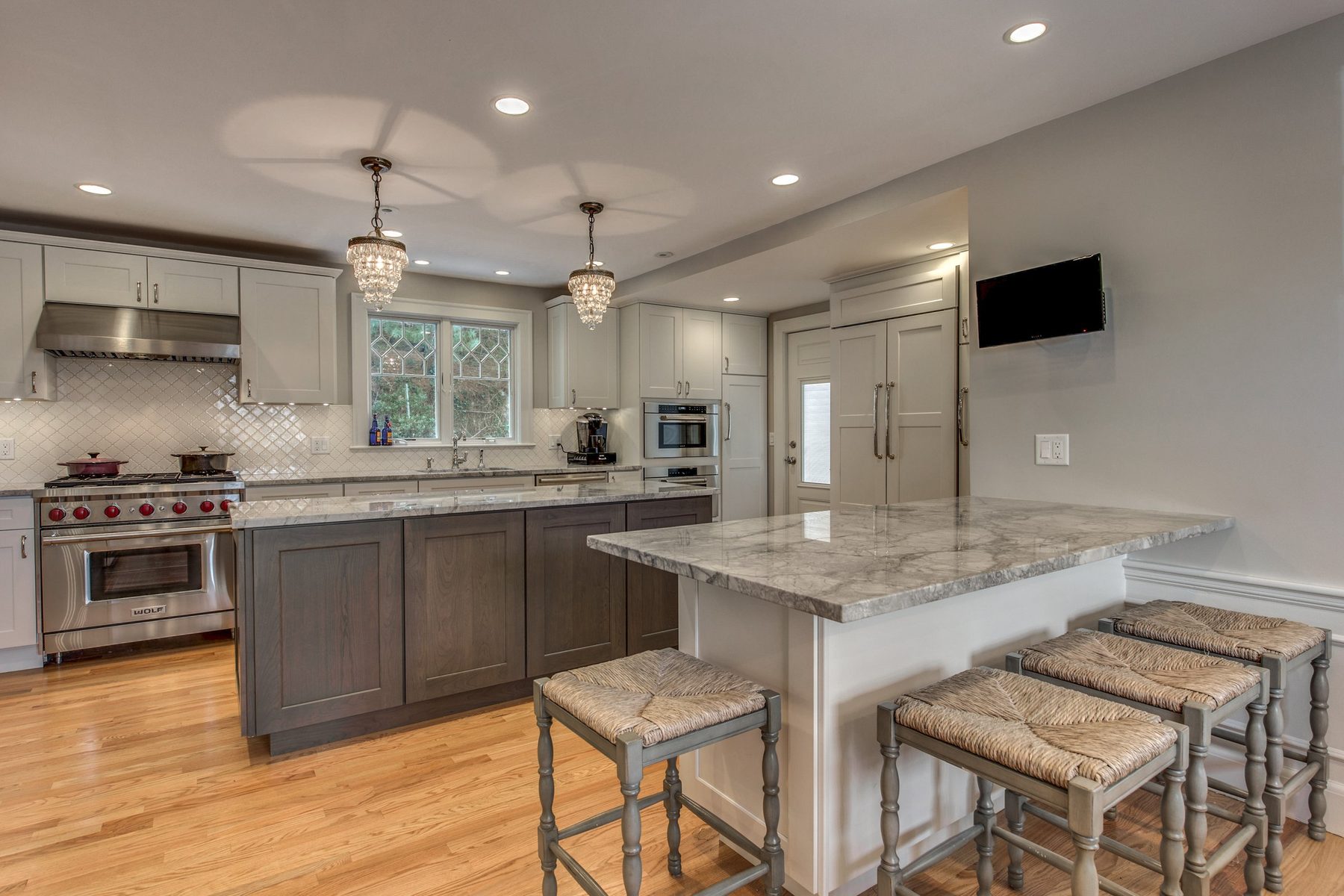 White Shaker kitchen with gray-stained island, peninsula seating and crystal pendants in Belmont, MA