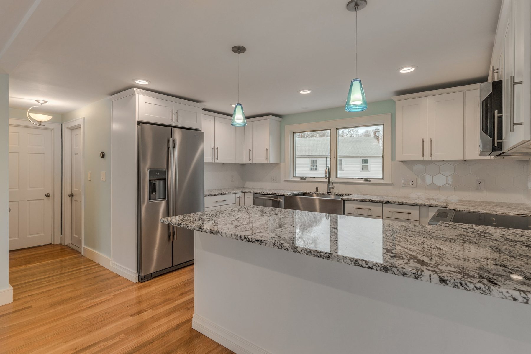 White Shaker kitchen with a peninsula, apron-front sink and blue glass pendants in Belmont, MA