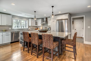 White shaker kitchen with a long charcoal island, white granite, woven counter stools and glass bell pendants in Lexington, MA