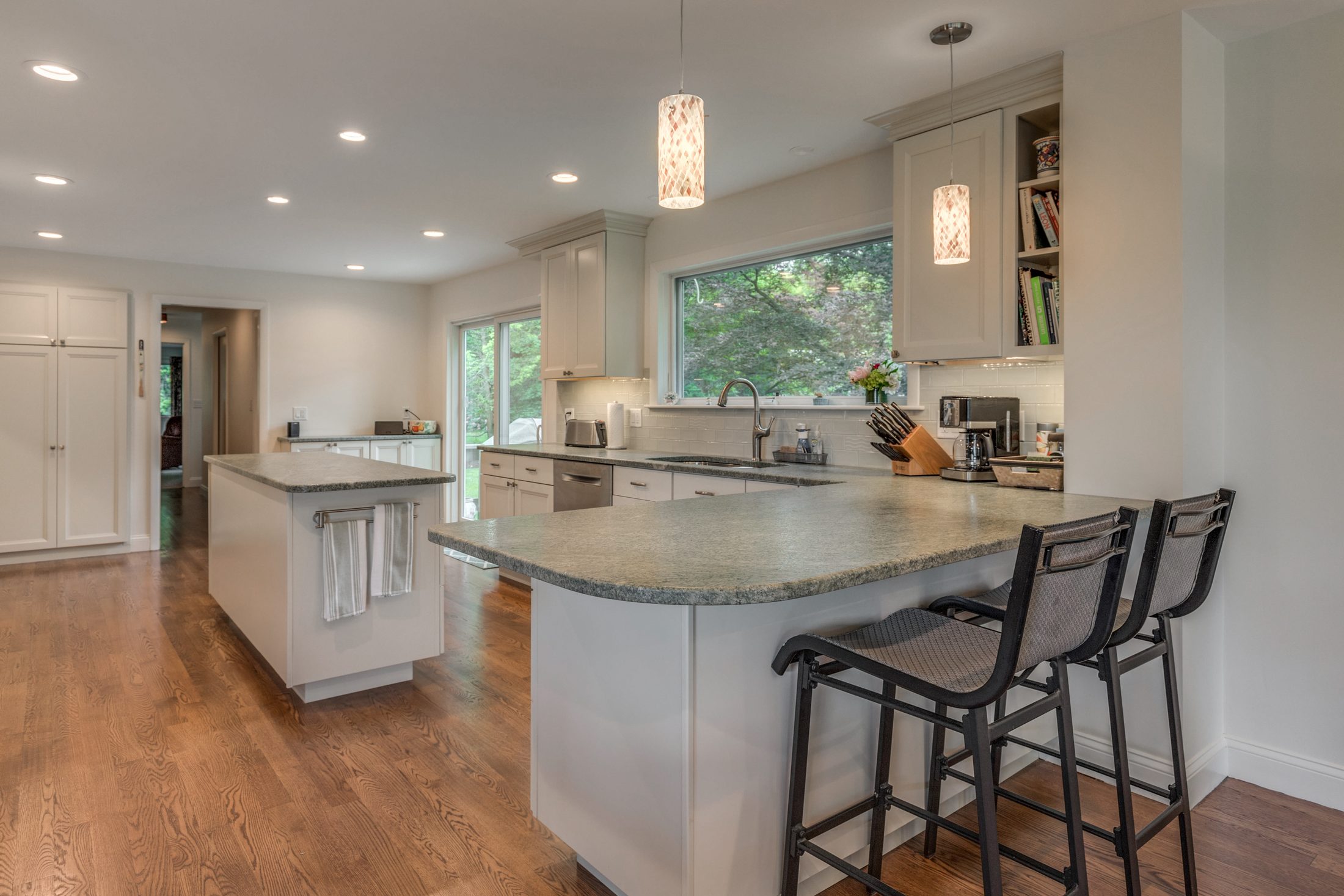 White shaker kitchen with green-gray stone counters, a curved peninsula with seating, a separate island and oak floors in Lexington, MA