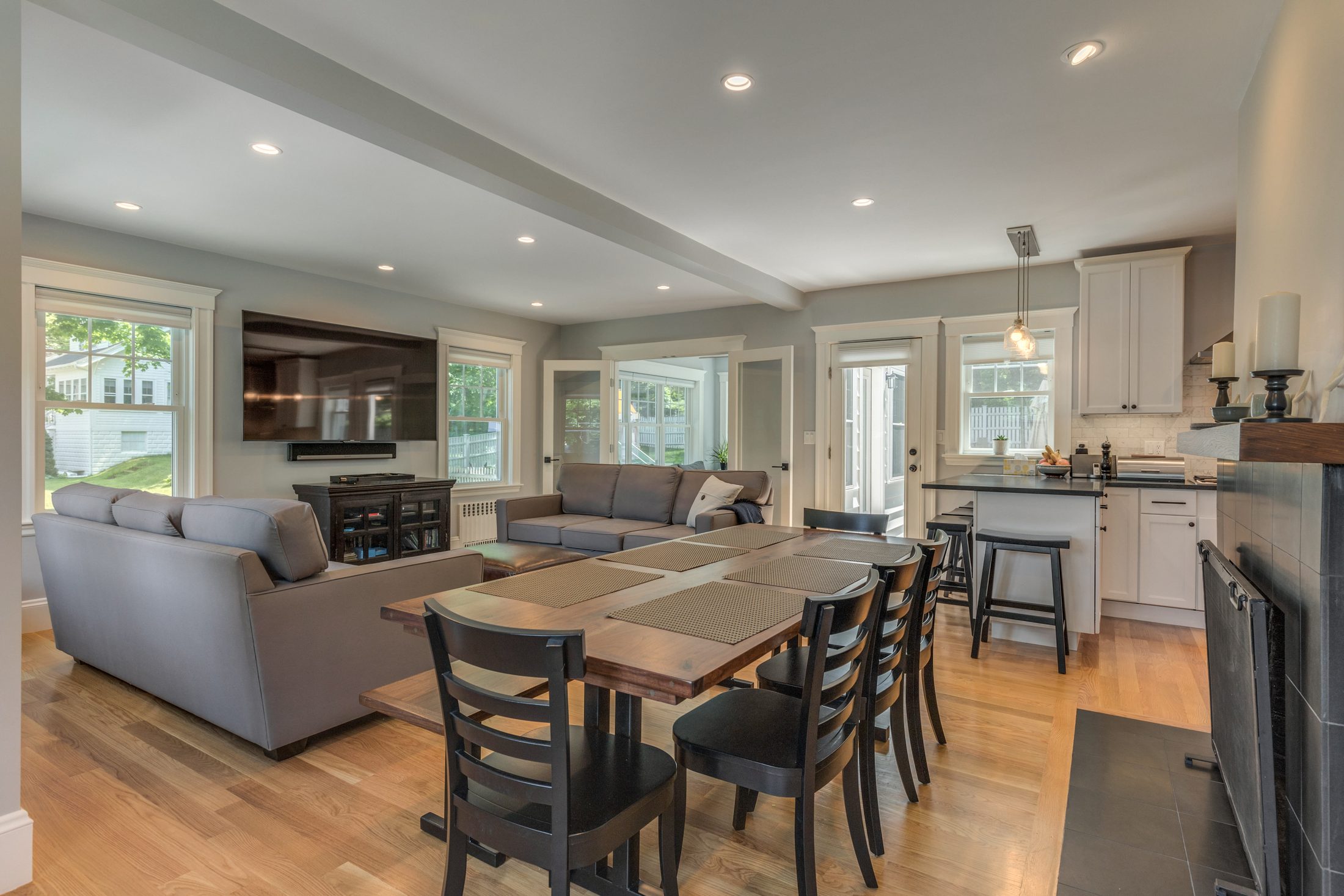 Open living and dining room with oak floors, a wall-mounted TV and a white shaker kitchen beyond in Lexington, MA