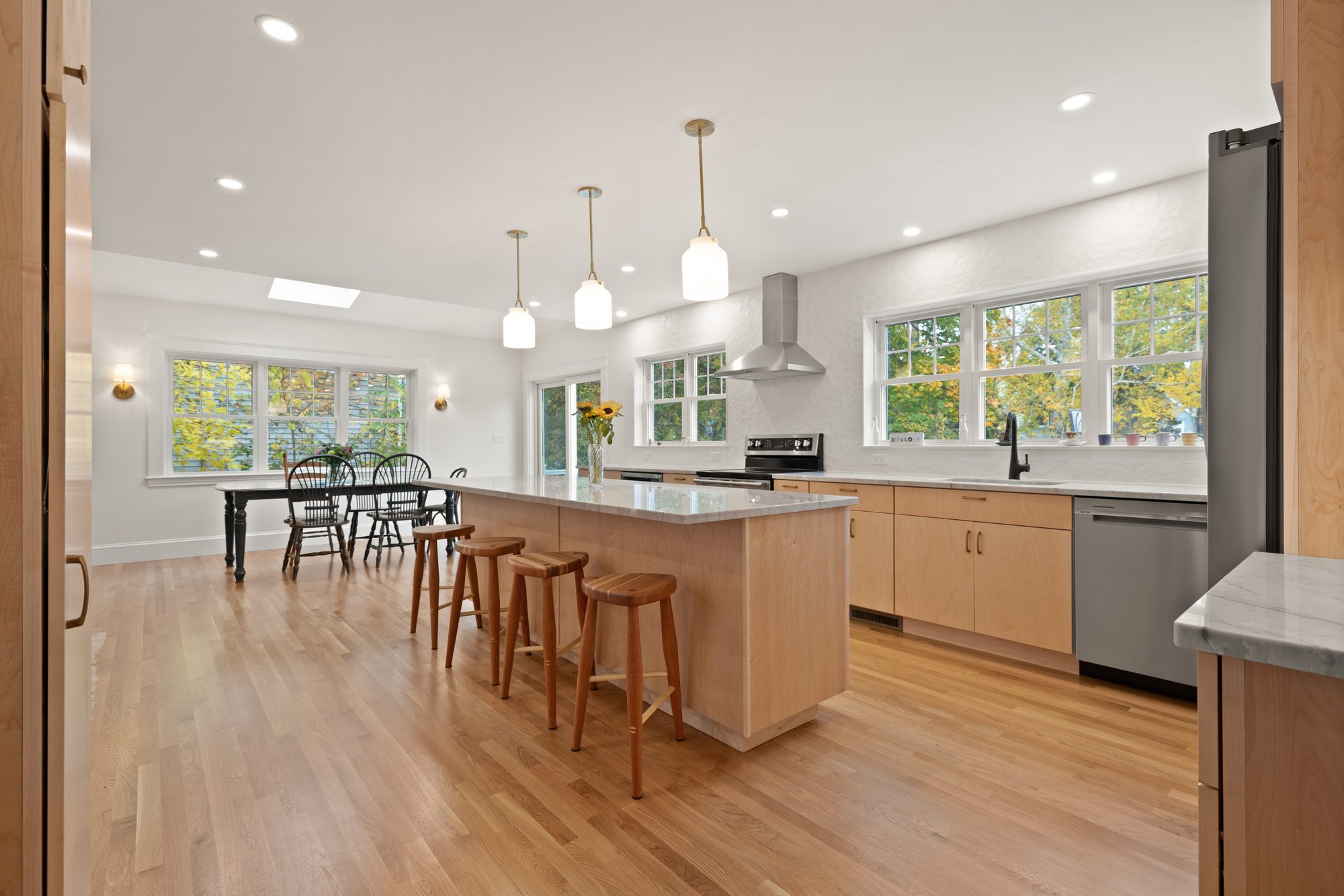 Long maple kitchen with an island, glass pendants and a skylit dining area in Melrose, MA