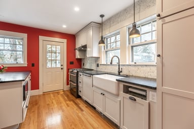 Remodeled kitchen in Melrose, MA with white shaker cabinets, black counters, farmhouse sink, marble hex backsplash and oak floors