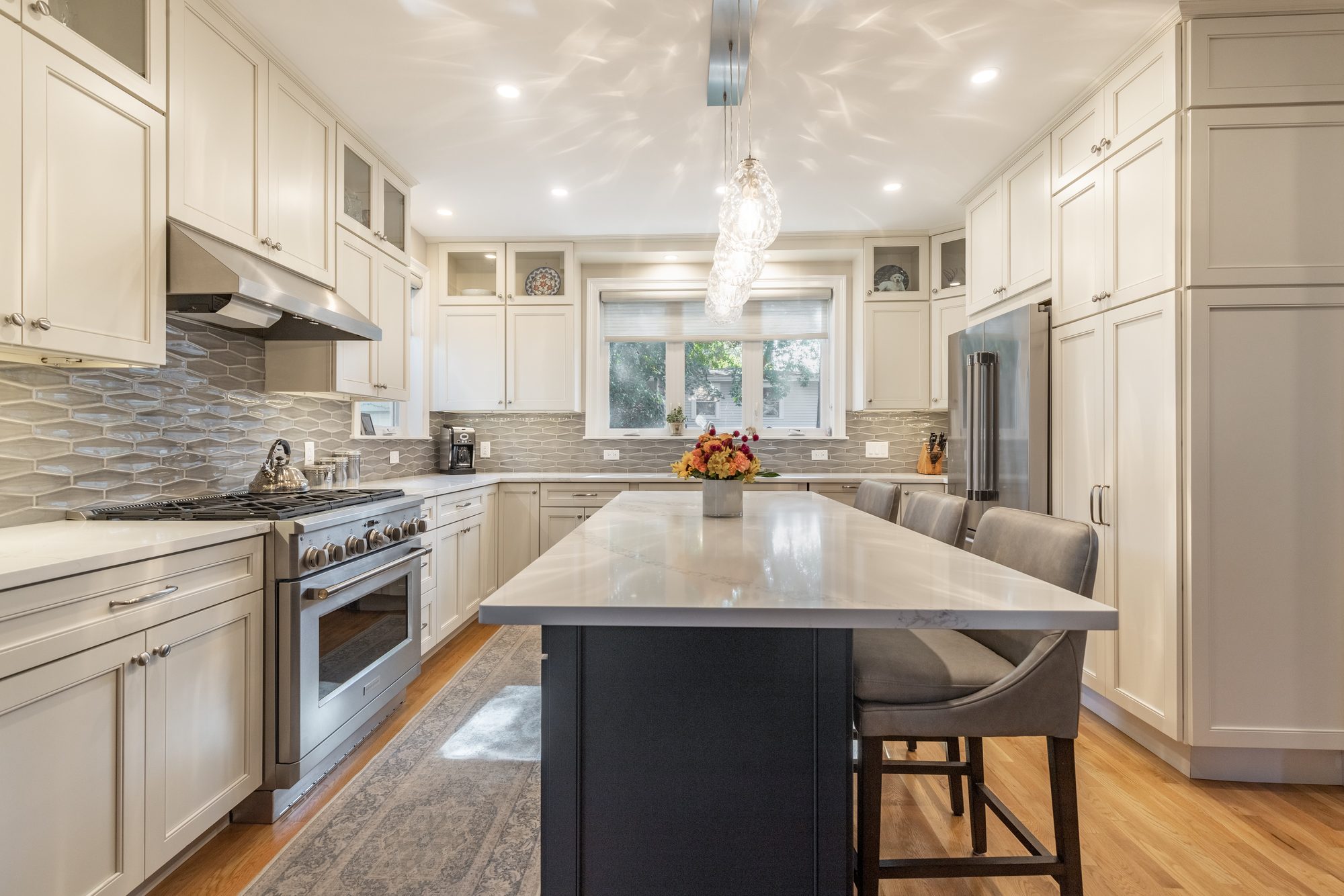 Open kitchen with white cabinets to the ceiling, navy island and pendant lights in Melrose, MA