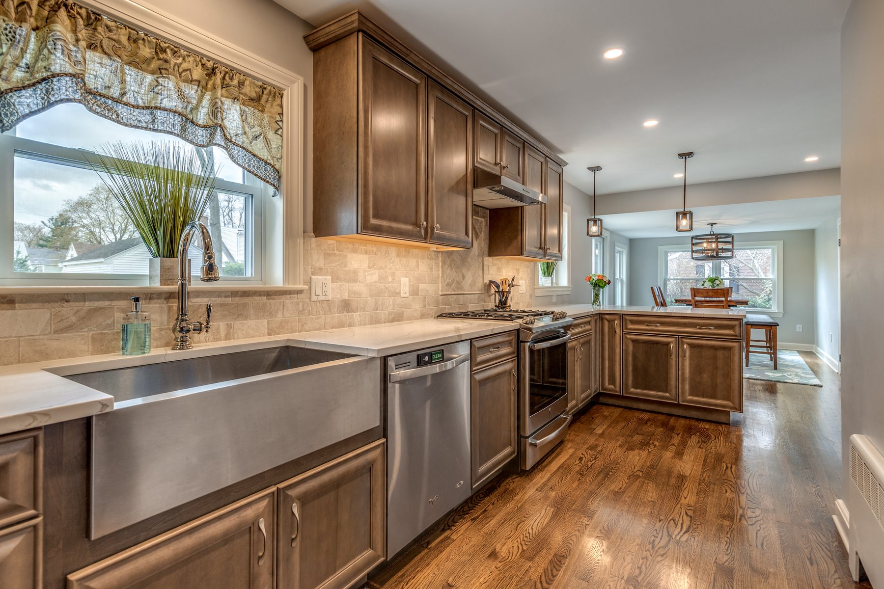 Kitchen in Wakefield, MA with stained maple cabinets, white quartz counters and a stainless farmhouse sink, open to a dining area