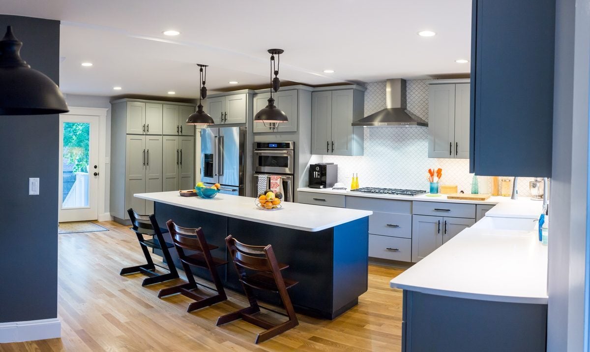 After: Kitchen: the range against the old brick chimney and the narrow doorway gave way to an open kitchen with a long navy island and seating.