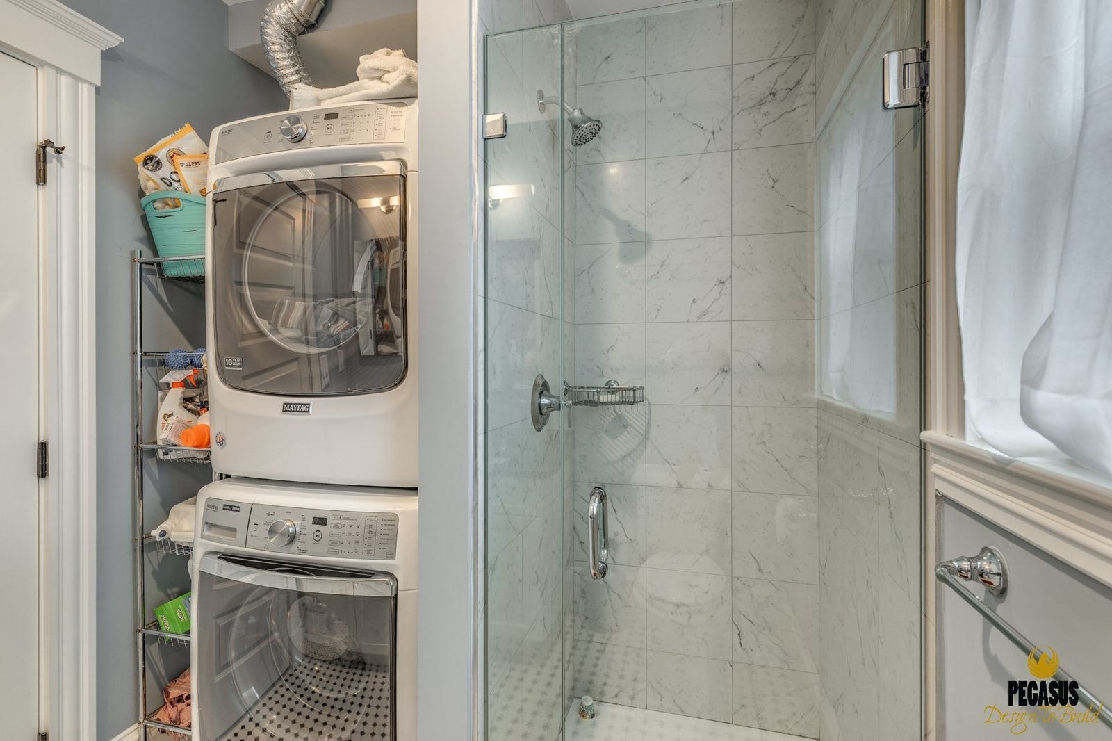 Laundry closet with stacked washer and dryer beside a marble-tiled glass shower in Arlington, MA