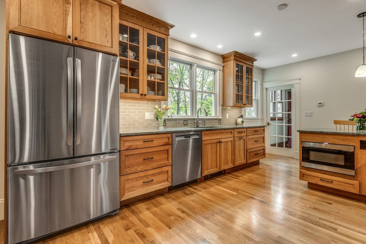 After: Fridge wall: the same spot, rebuilt with cherry glass-front uppers and a full sink run under new windows.