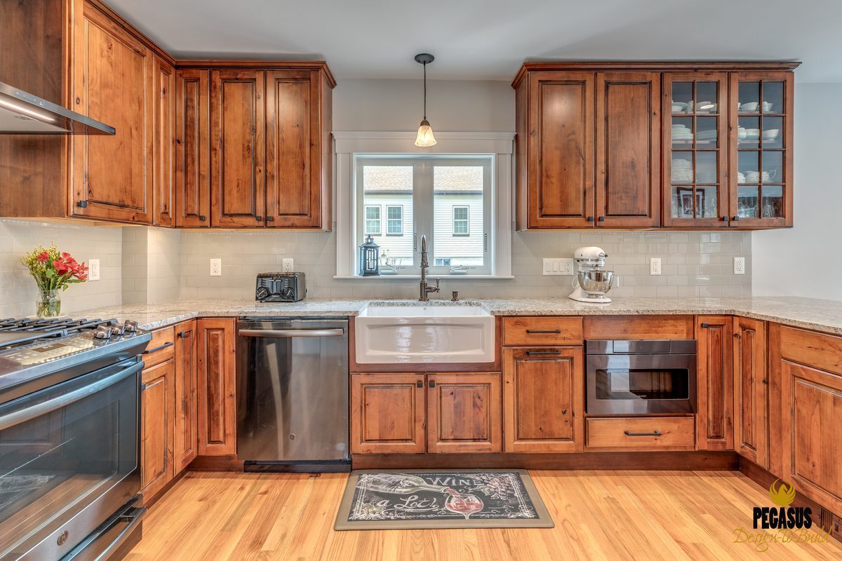 After: Sink wall: dark oak cabinets, laminate counters and a drop-in cooktop gave way to rustic alder cabinets, granite counters, a fireclay farmhouse sink and a subway tile backsplash.