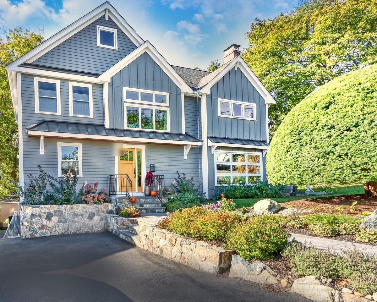 After: From the driveway: a one-story ranch became a full two-story home with board-and-batten gables, a metal-roofed entry and a new stone-walled front walk.