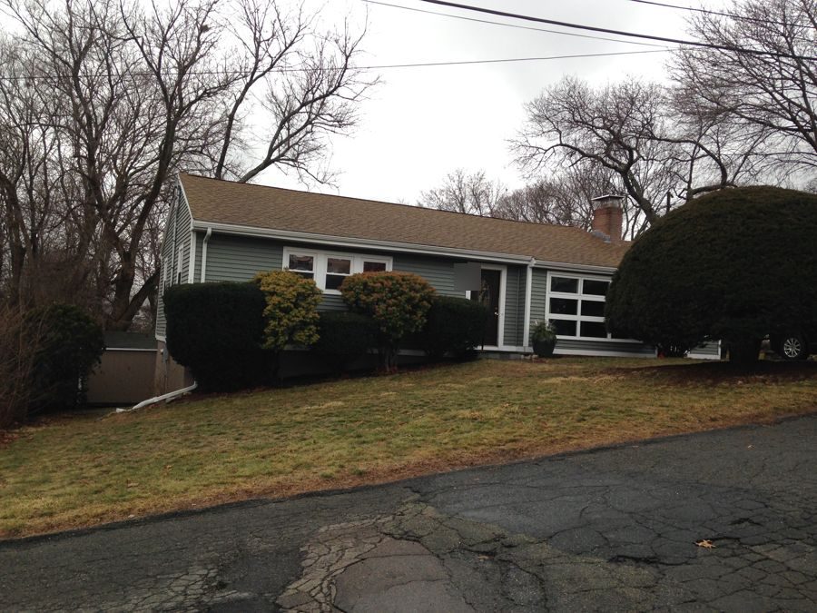 Before: From the driveway: a one-story ranch became a full two-story home with board-and-batten gables, a metal-roofed entry and a new stone-walled front walk.