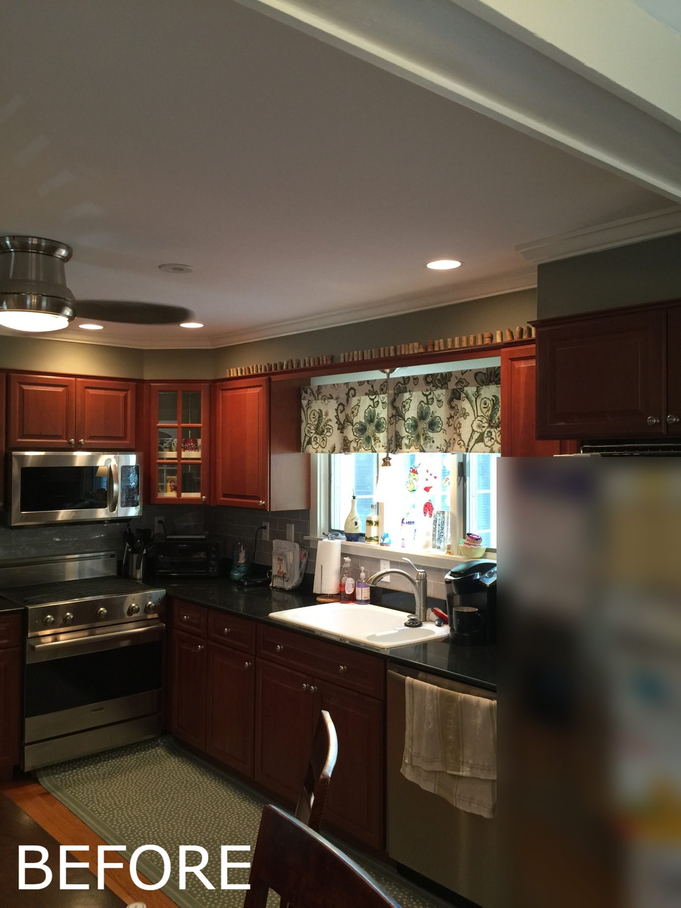 Before: Sink wall: dark cabinets and black counters replaced by white Shaker cabinets, quartz counters, a pro range and hood, tile backsplash and a new leaded-glass window.