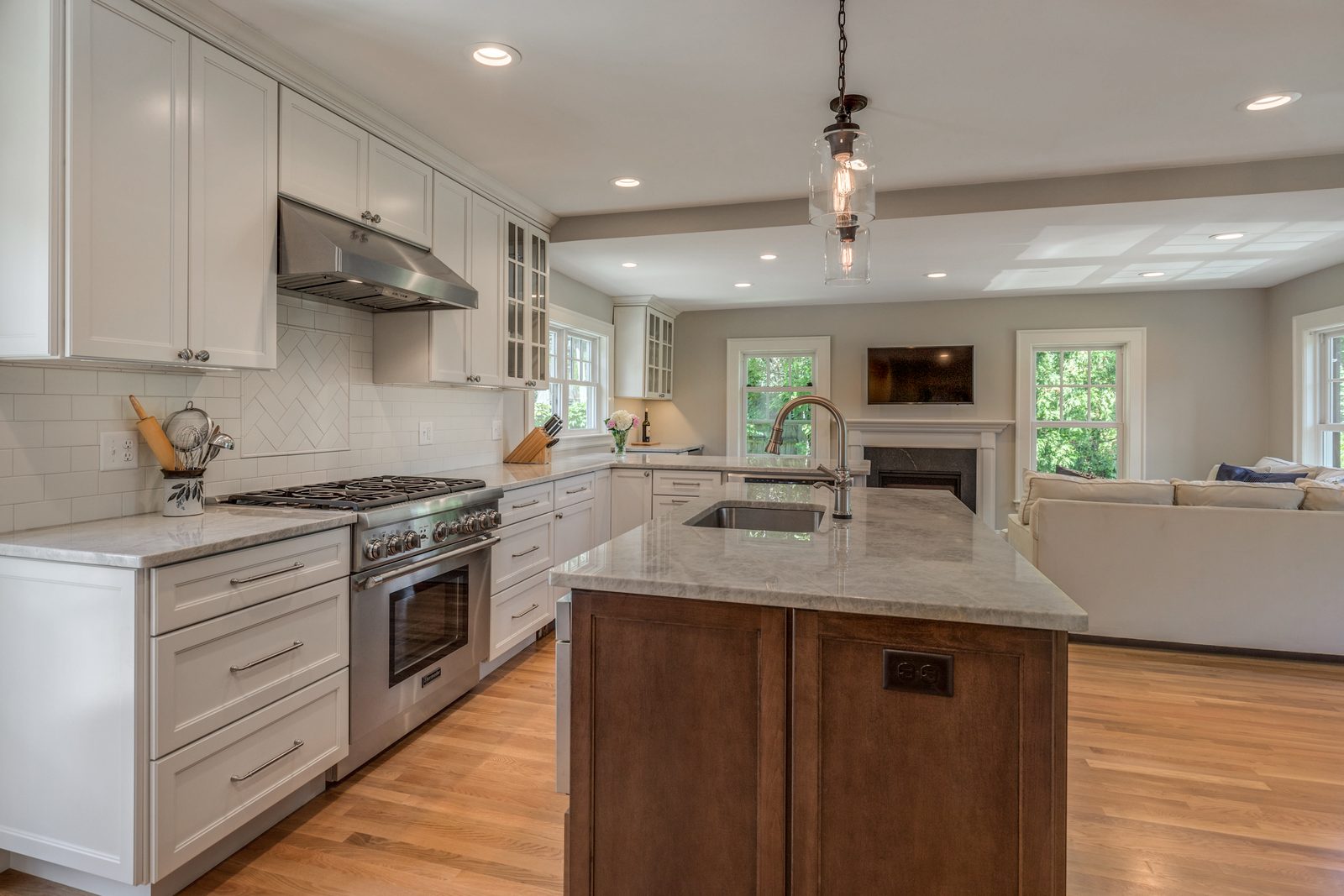Belmont, MA kitchen opened to the family room, with white cabinets, wood island and fireplace beyond