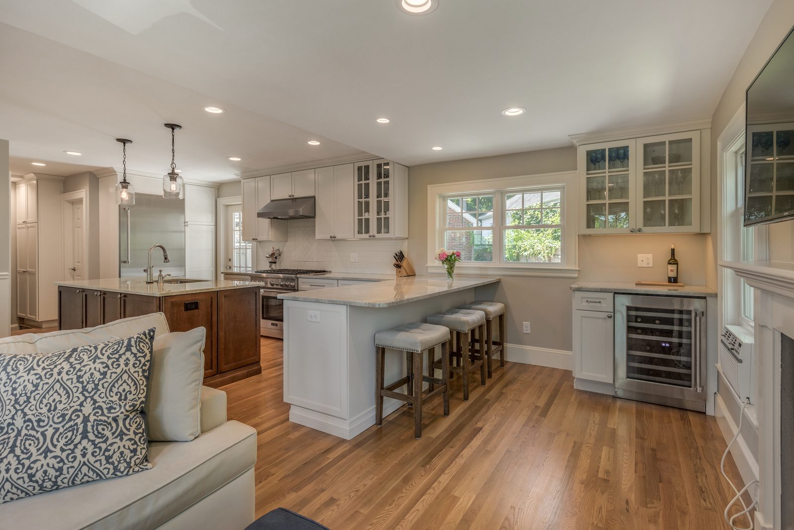 View from the family room into the open kitchen in Belmont, MA with peninsula seating, wine fridge and glass-front cabinets