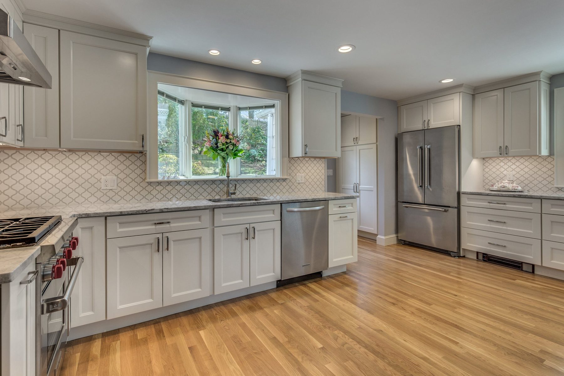 Sink under a bay window with stainless appliances and arabesque tile backsplash in Belmont, MA