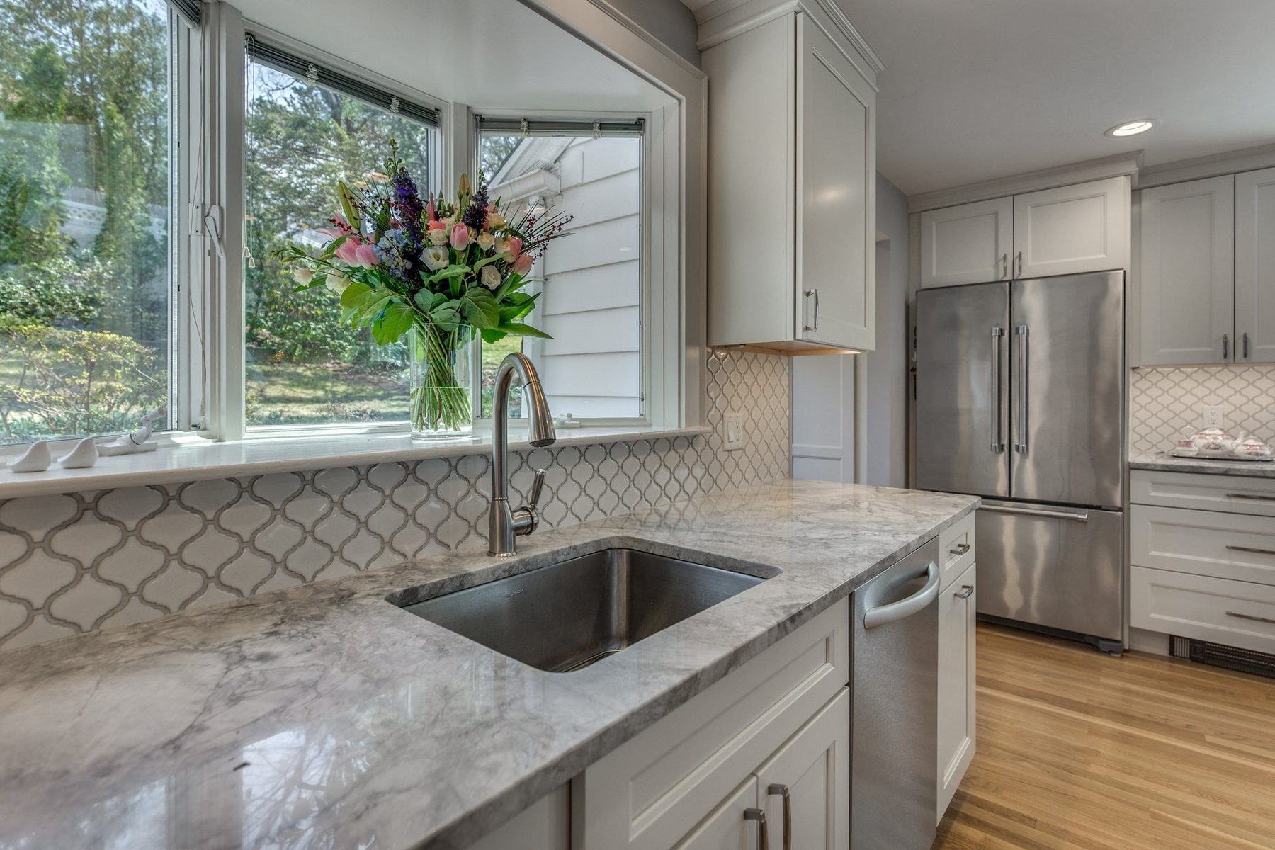 Undermount sink and gray-veined stone counters below a bay window in Belmont, MA