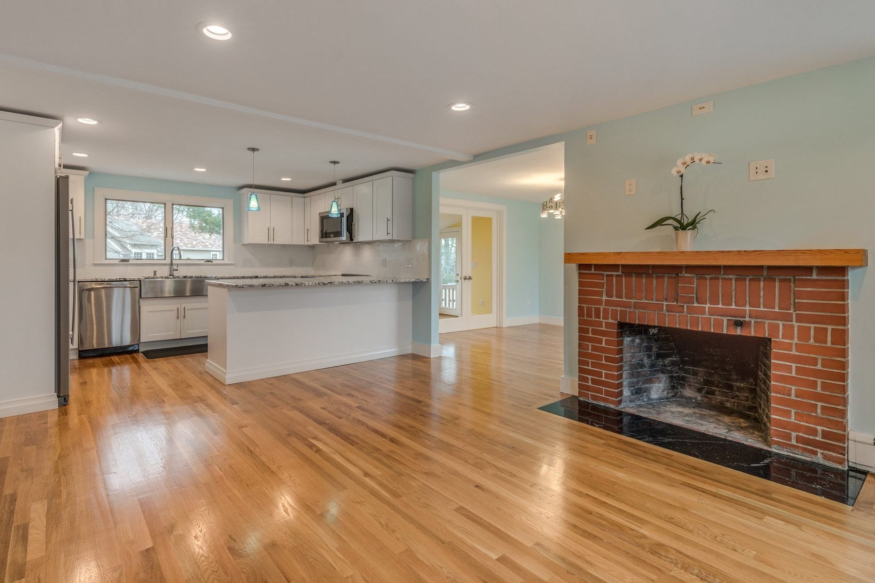 Open kitchen and living room with oak floors and a brick fireplace in Belmont, MA