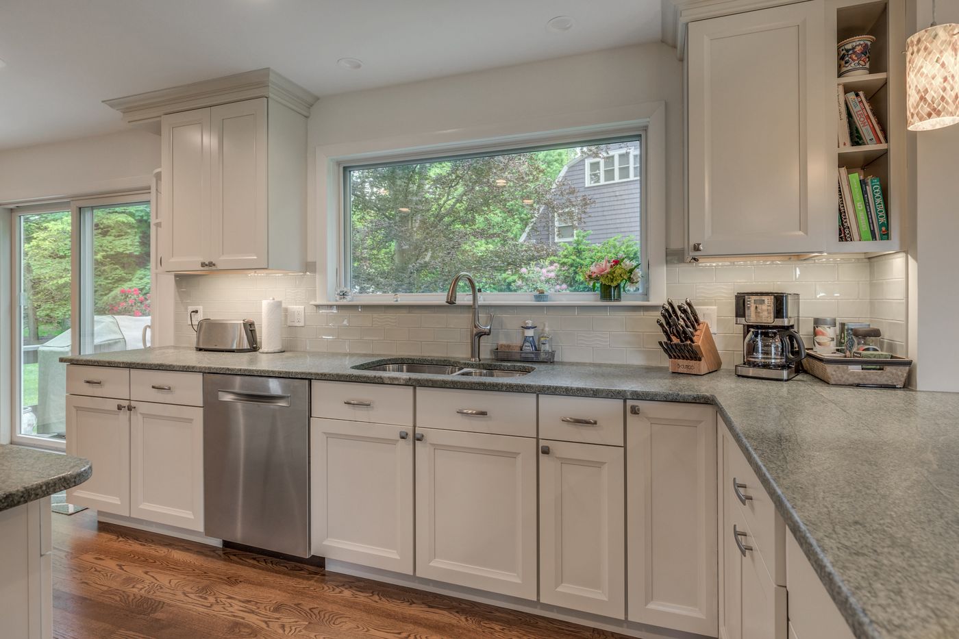 After: Kitchen sink wall: dark cabinets and a valance-covered window gave way to white shaker cabinets, green-gray stone counters and an open view over the sink.