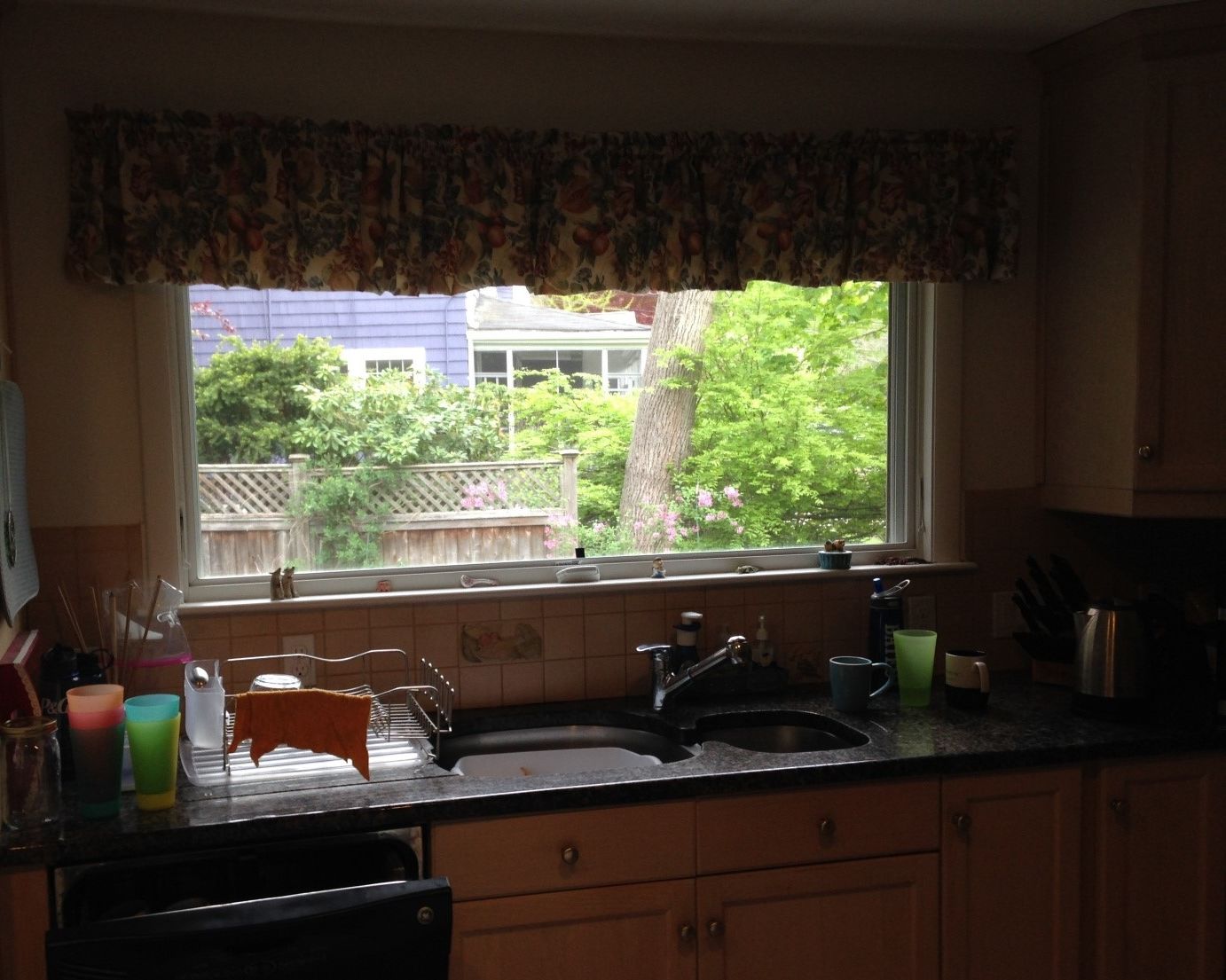 Before: Kitchen sink wall: dark cabinets and a valance-covered window gave way to white shaker cabinets, green-gray stone counters and an open view over the sink.