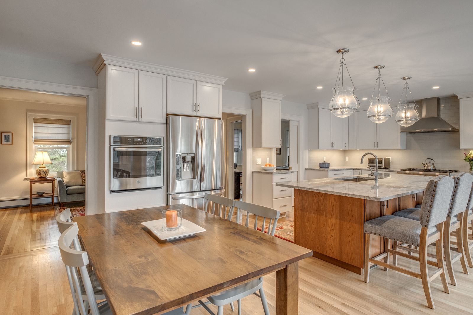 Dining table in the open kitchen with stainless wall oven, refrigerator and island seating