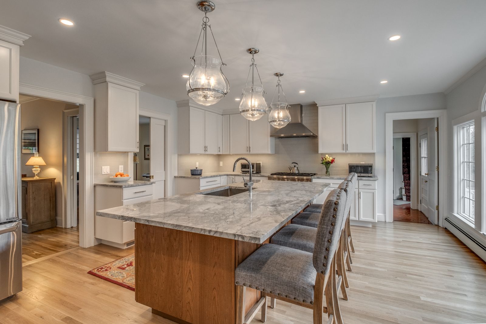 Wood island with stone top and bar seating, looking down the length of the open kitchen