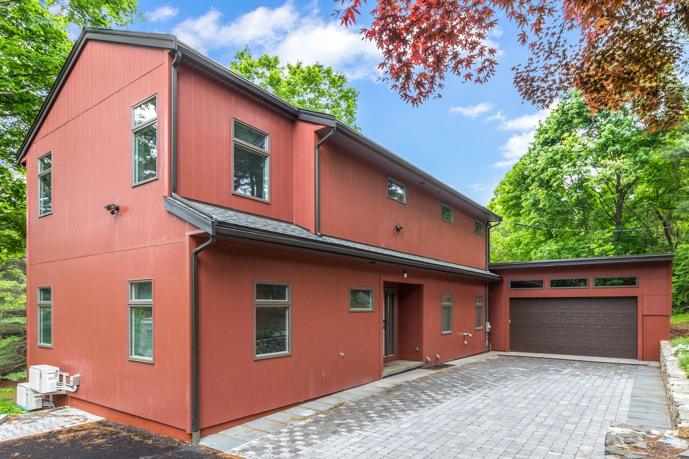 After: Front: a low gray ranch tucked behind the trees became a two-story home with new siding, a new front entry, a garage and a paver driveway.