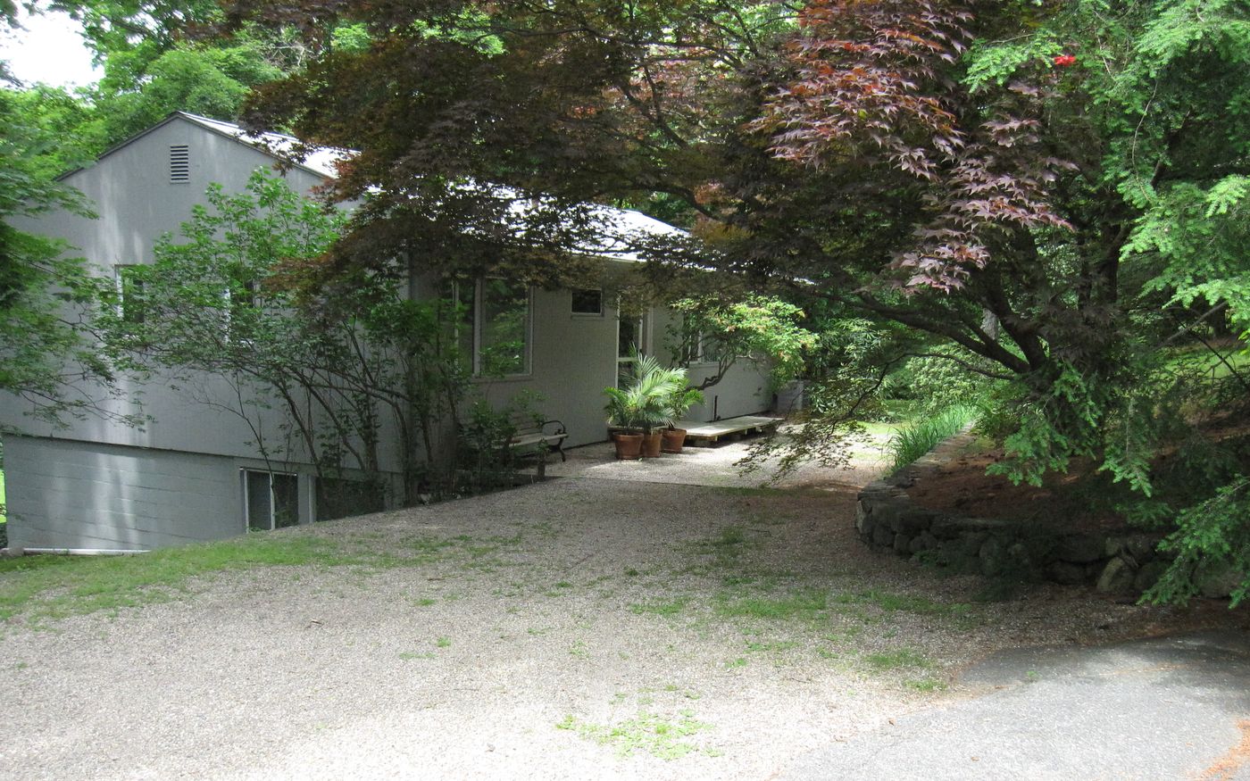 Before: Front: a low gray ranch tucked behind the trees became a two-story home with new siding, a new front entry, a garage and a paver driveway.