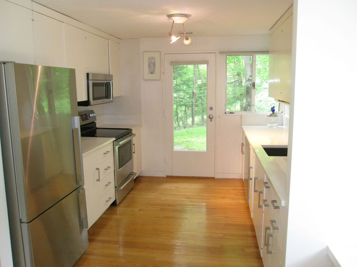 Before: Kitchen: a narrow white galley kitchen gave way to an open kitchen with maple cabinets, an island and a wall of glass to the trees.