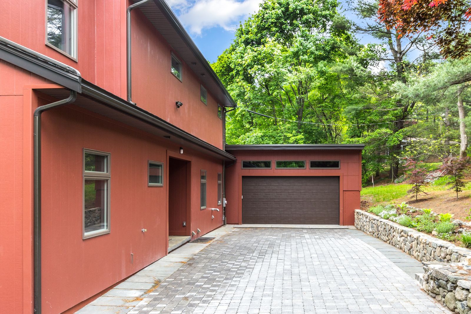 New garage with transom windows at the end of a paver driveway and stone retaining wall
