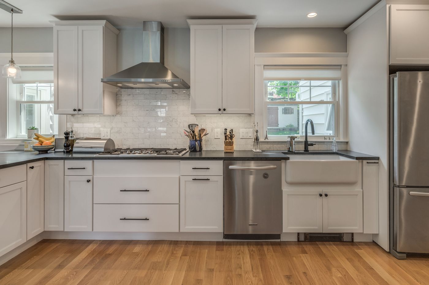 After: Kitchen: the sink stayed under the back window, with new shaker cabinets, a marble backsplash, a gas cooktop and a stainless hood.