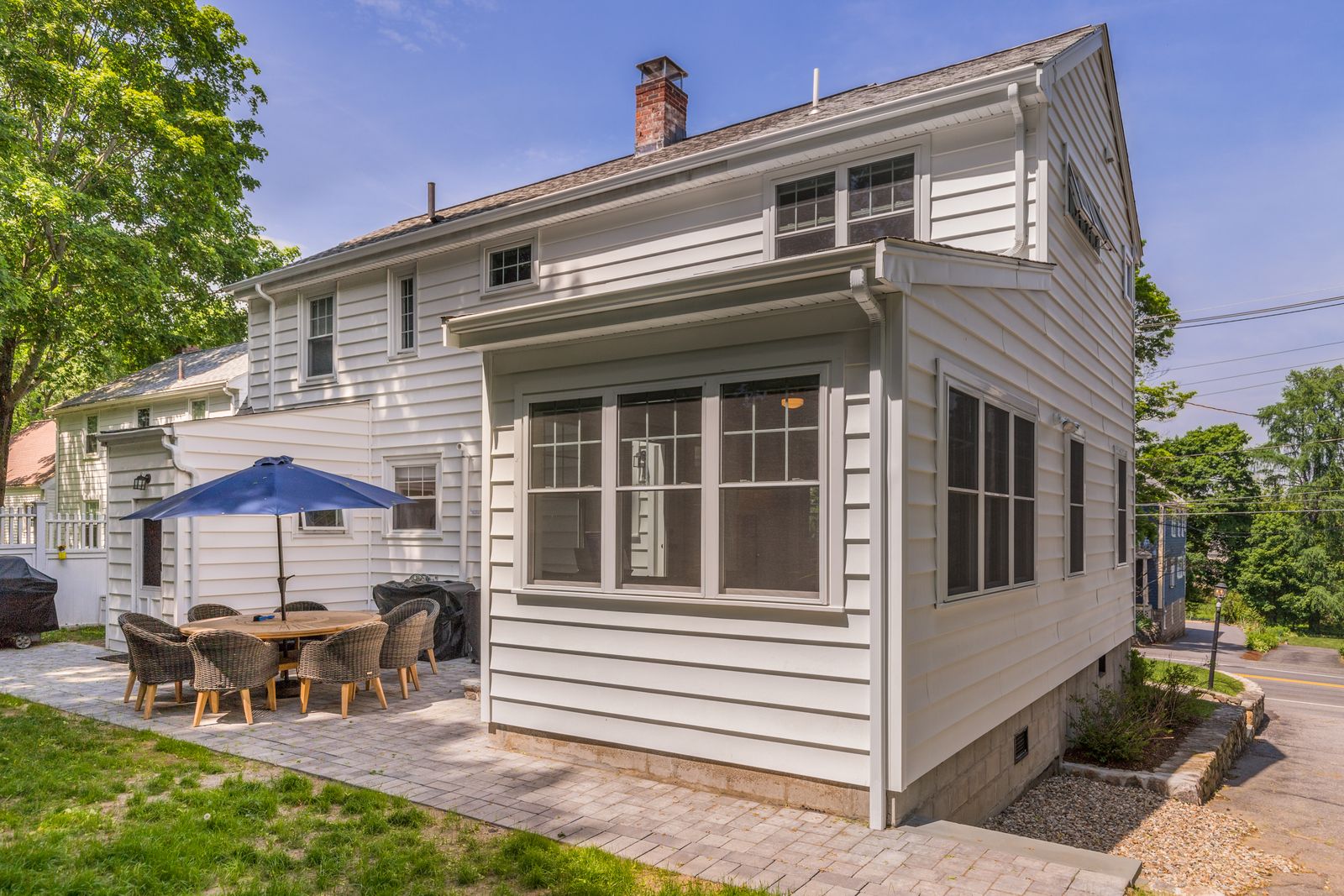 Back of the white colonial with the new sunroom bump-out and a paver patio