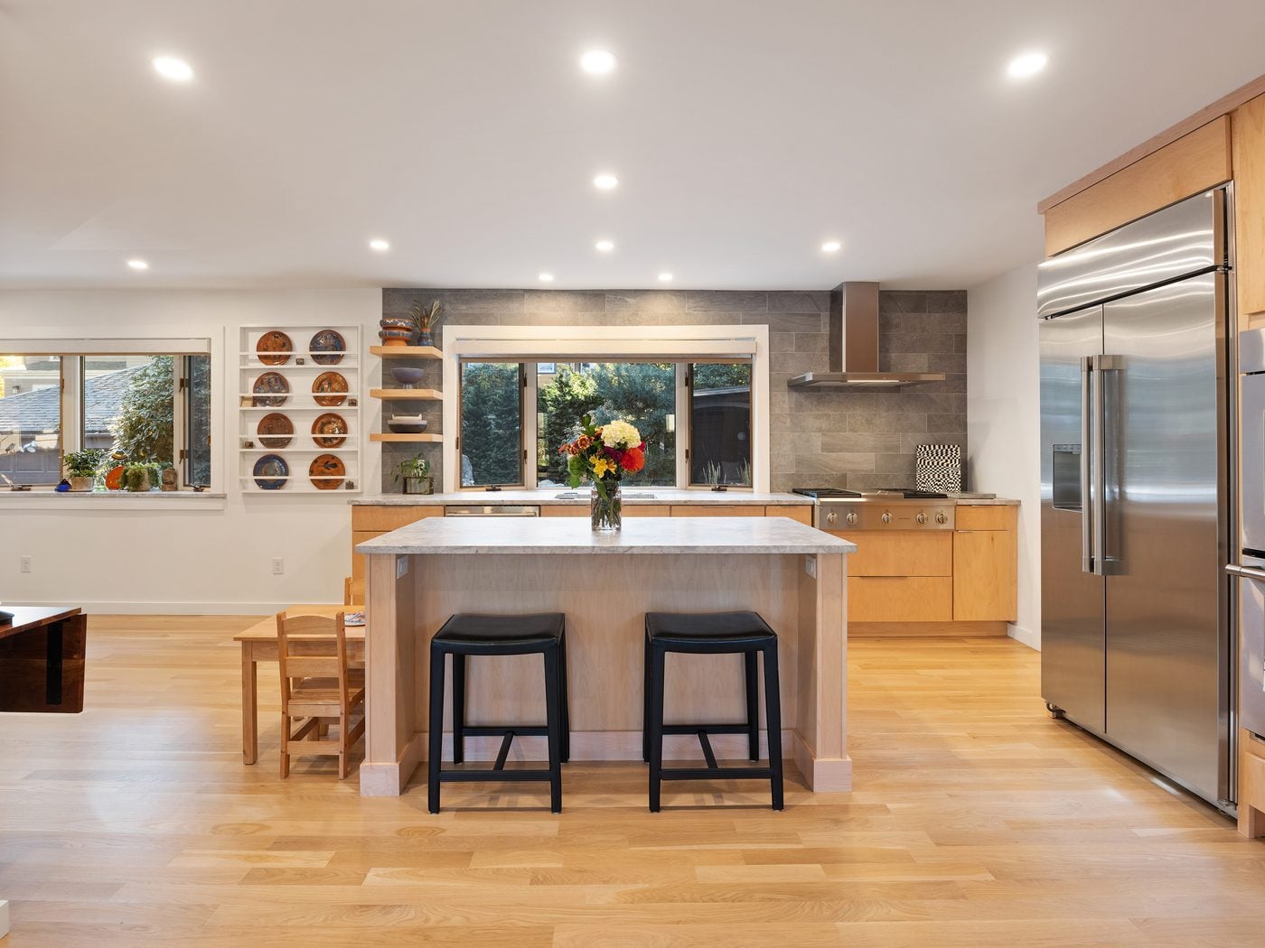 After: Kitchen: painted cabinets and a freestanding range gave way to natural maple flat-panel cabinets, a stone-topped island and a gas rangetop under a chimney hood, with the sink still facing the garden.