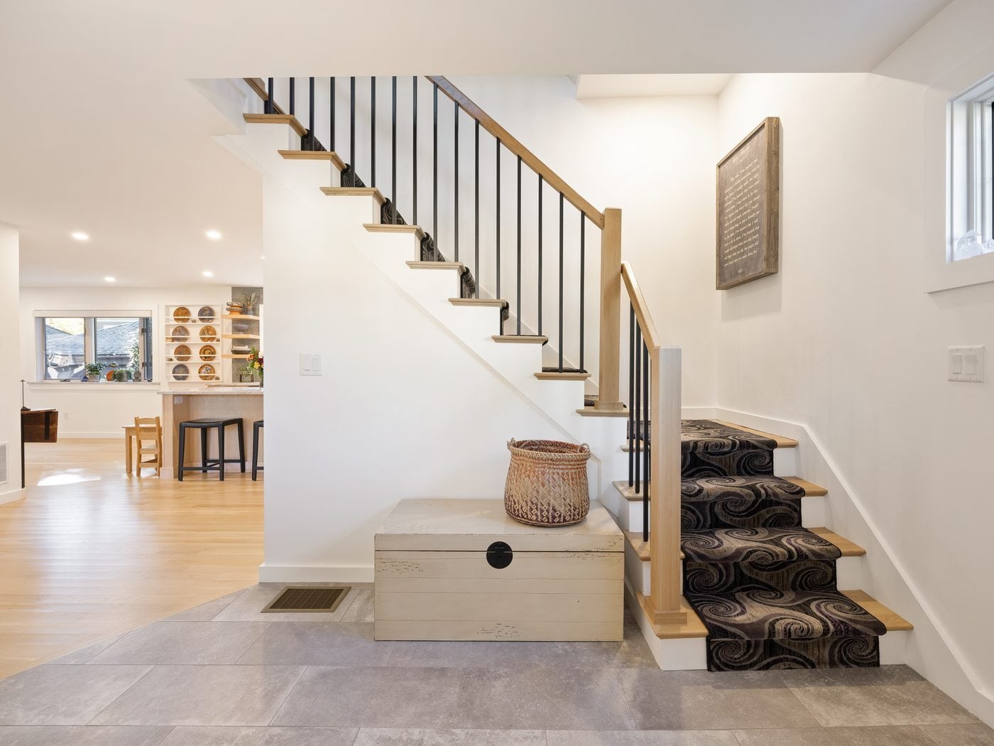 After: Front hall: the closed-in entry now opens to the kitchen, with a rebuilt stair of oak treads and black balusters and a tile floor.