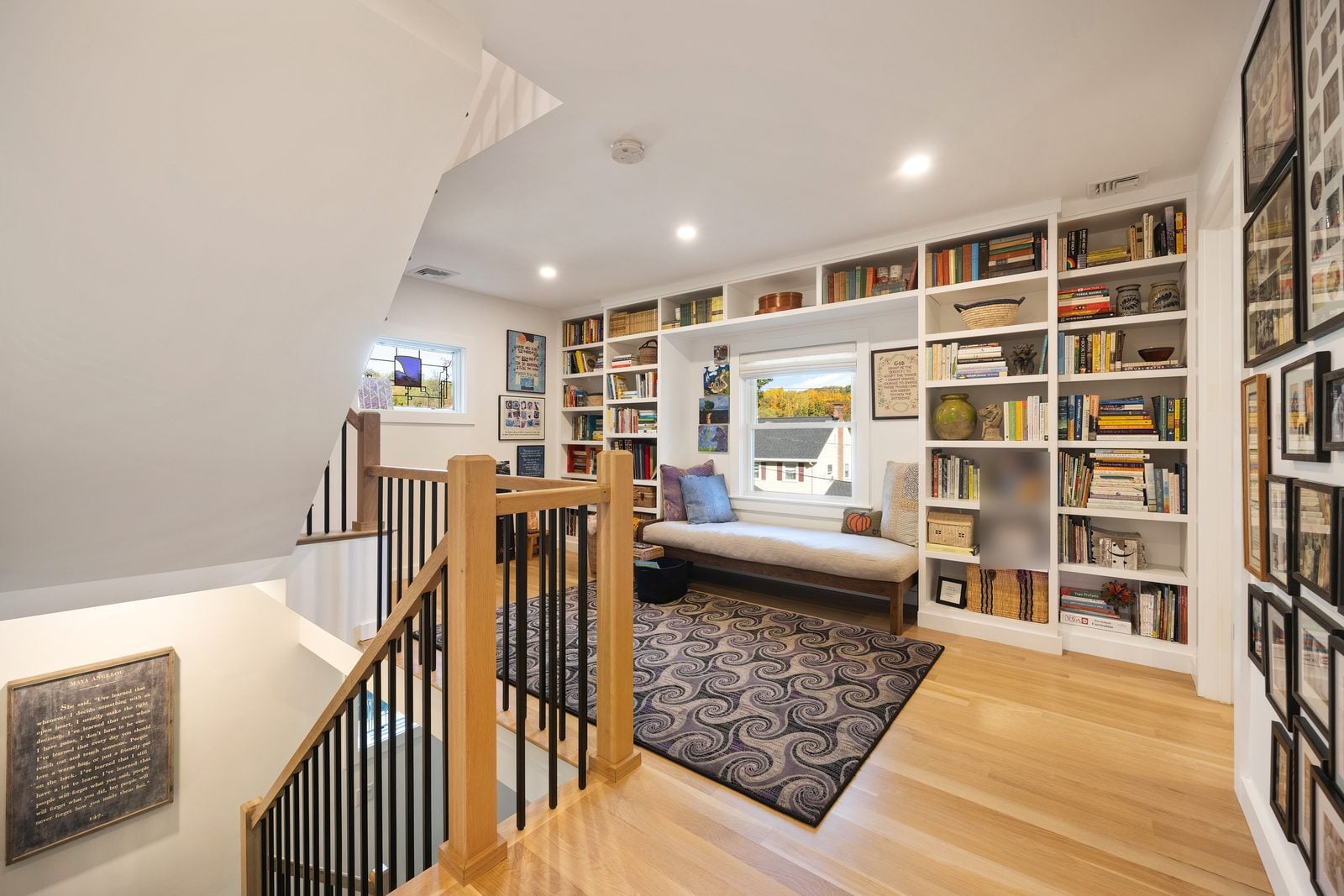 Second-floor landing with built-in bookshelves around a window seat and an oak and black baluster stair rail