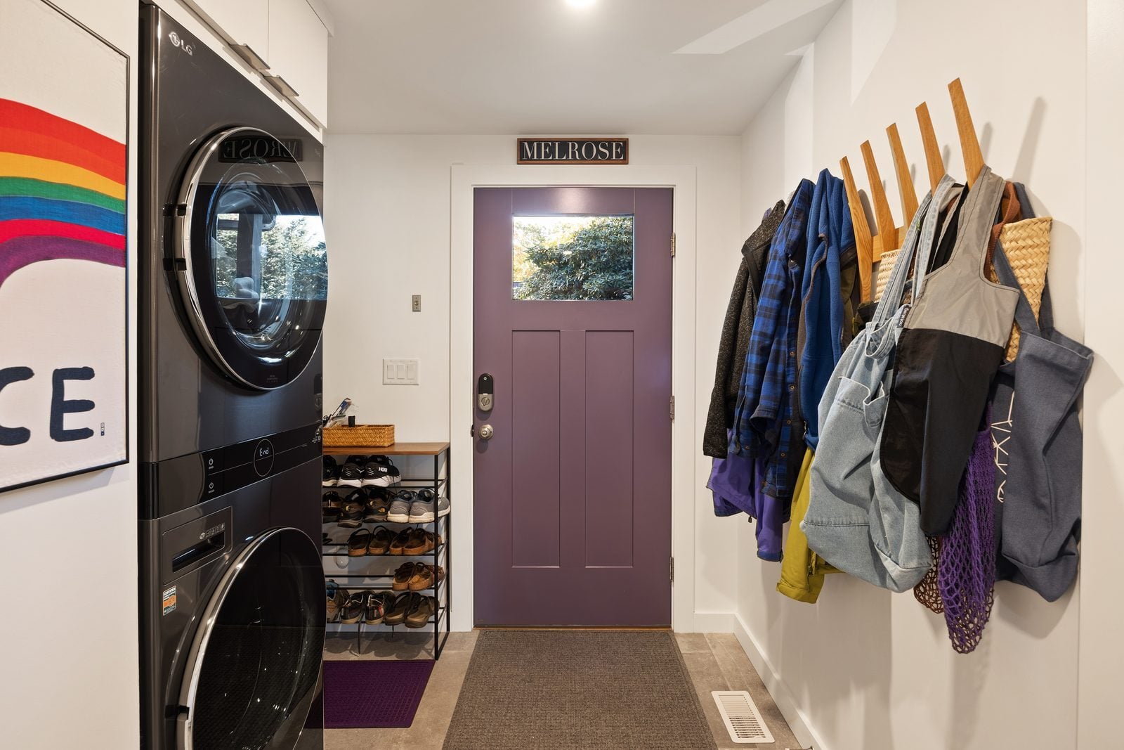 Rear mudroom with stacked washer and dryer, coat pegs and a purple back door