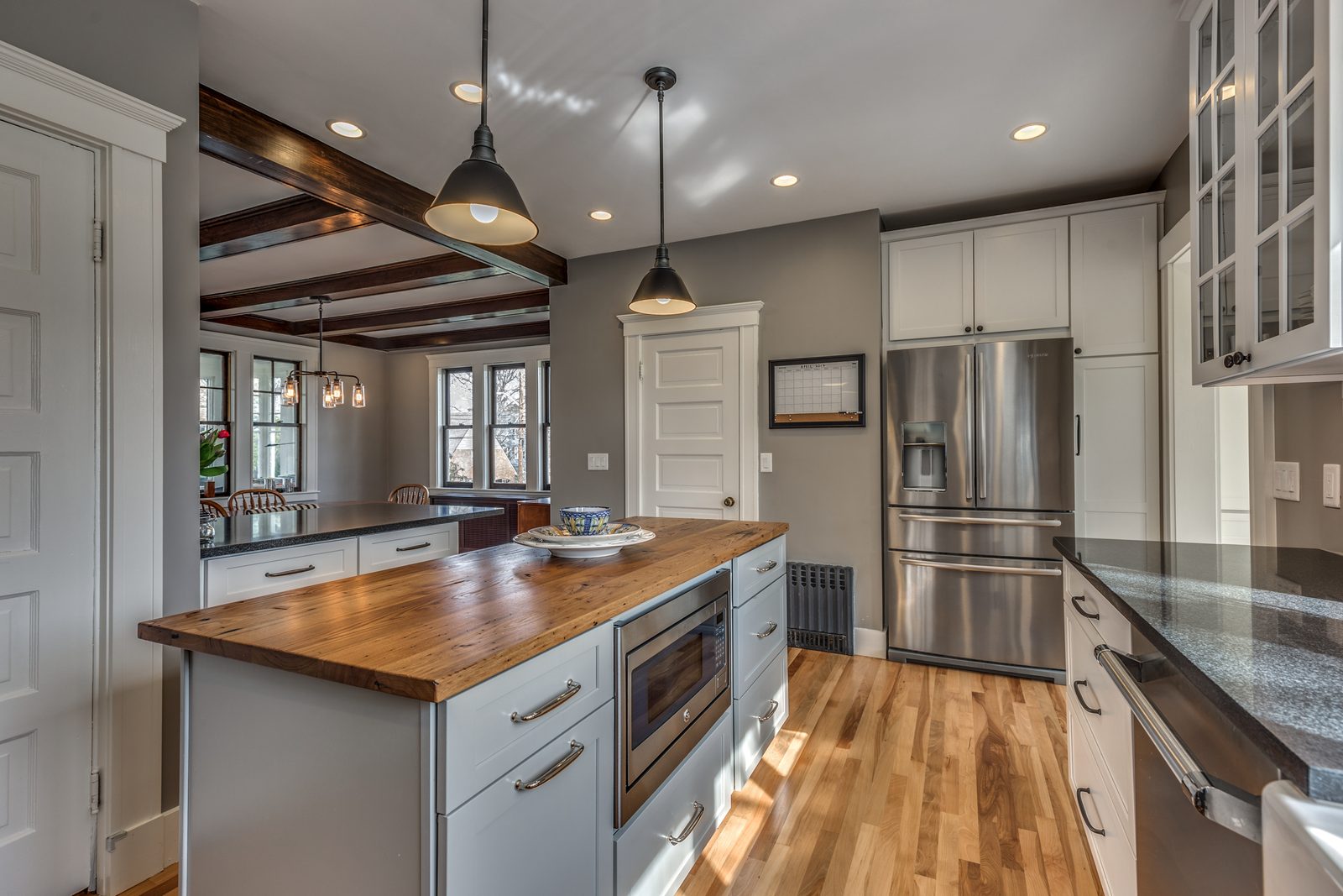 Gray island with reclaimed wood top and microwave drawer, stainless refrigerator and beamed dining room beyond