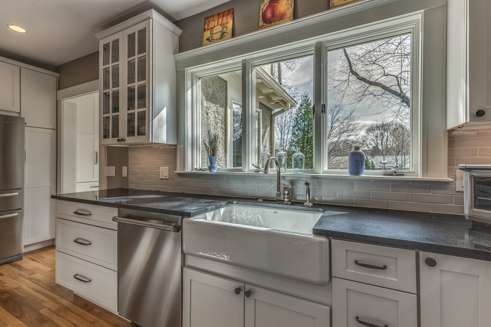 Farmhouse sink under a new triple window with glass-front upper cabinets