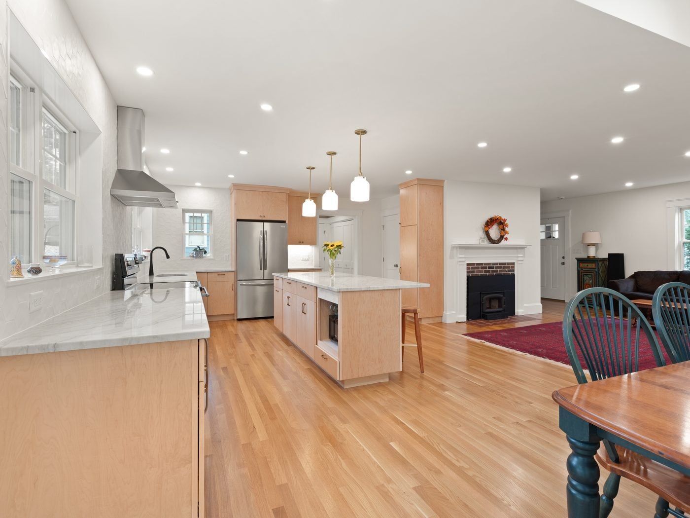 After: Kitchen: a small L-shaped kitchen with dark cabinets and a drop ceiling became a long, bright kitchen with maple cabinets, an island and windows over the counters.
