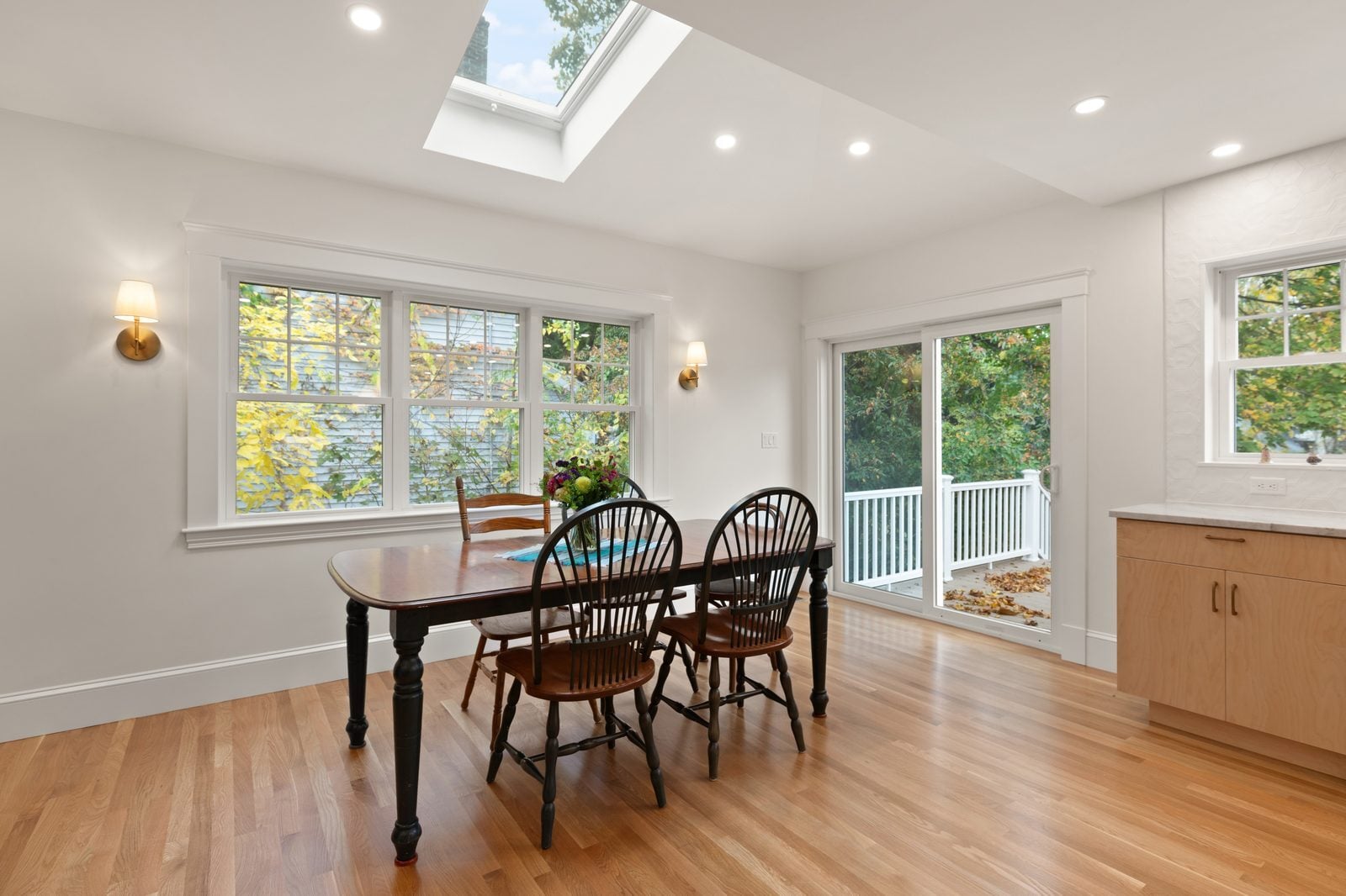 Dining area with a vented skylight in the vaulted ceiling, brass sconces and a slider to the deck
