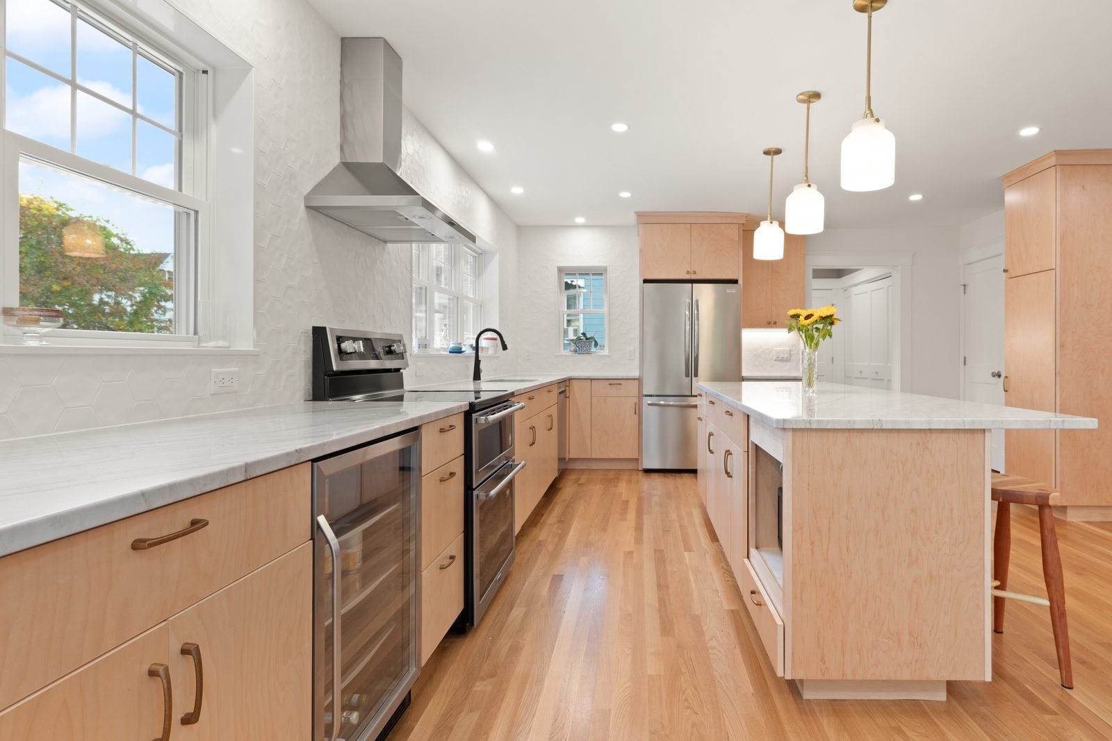 Long kitchen run with a stainless hood, white textured hex tile and a counter-depth refrigerator
