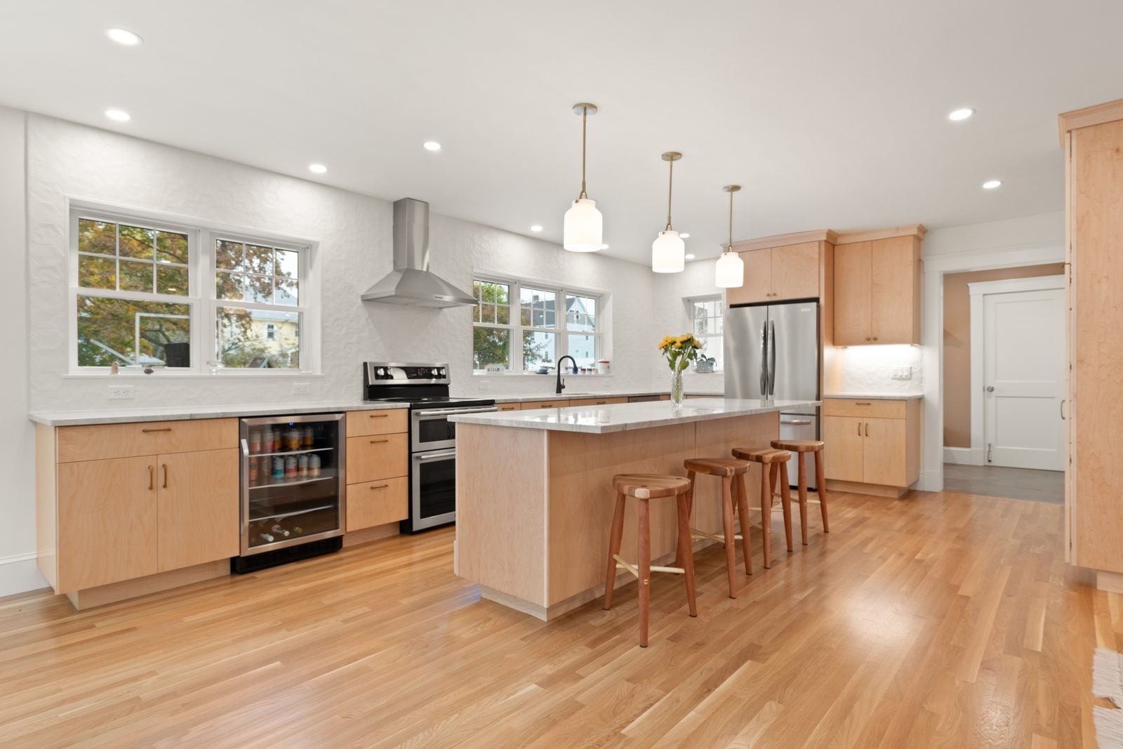 Kitchen island with four stools, beverage fridge and double-oven range along the window wall