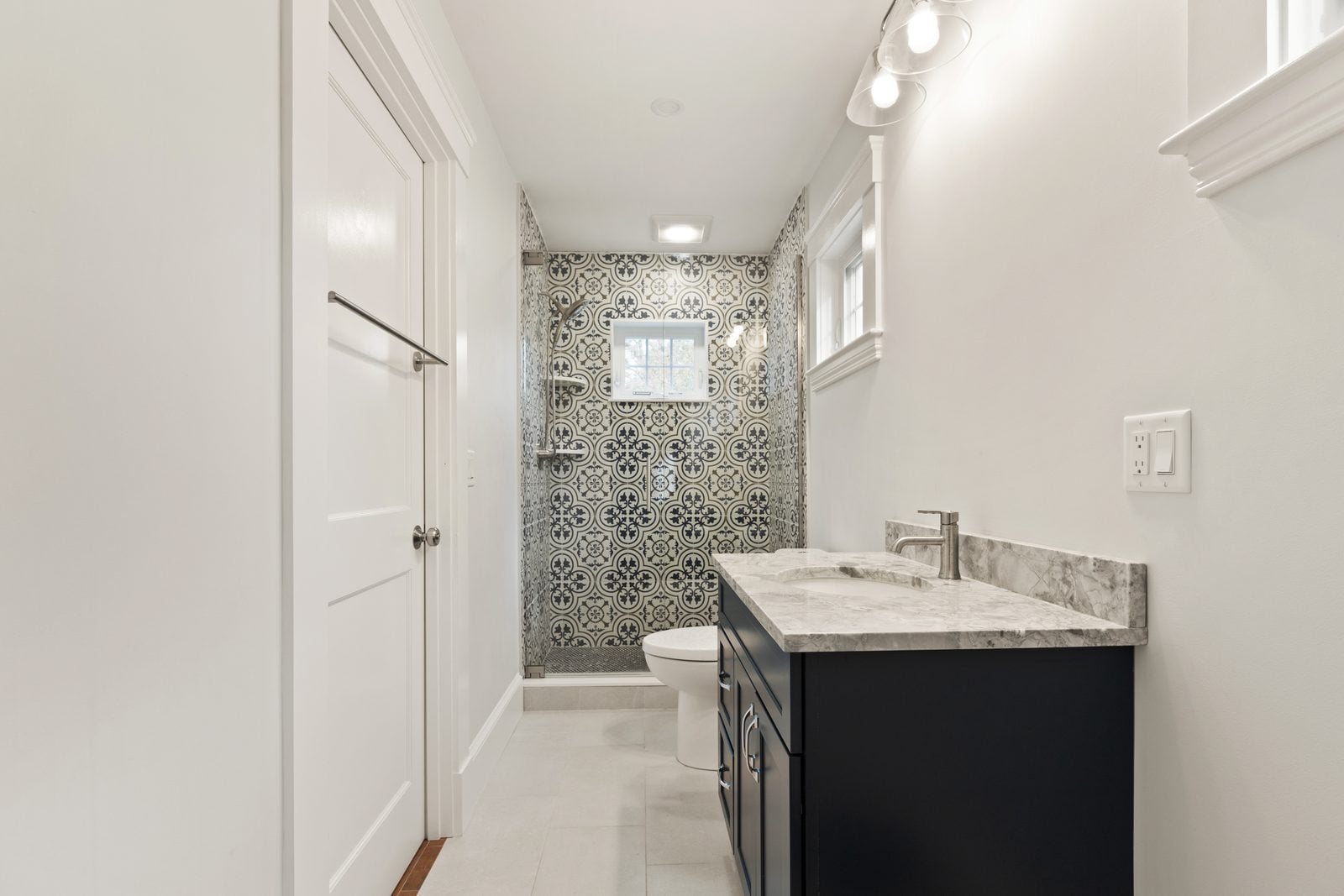 Bathroom with a navy shaker vanity, gray stone top and patterned tile shower