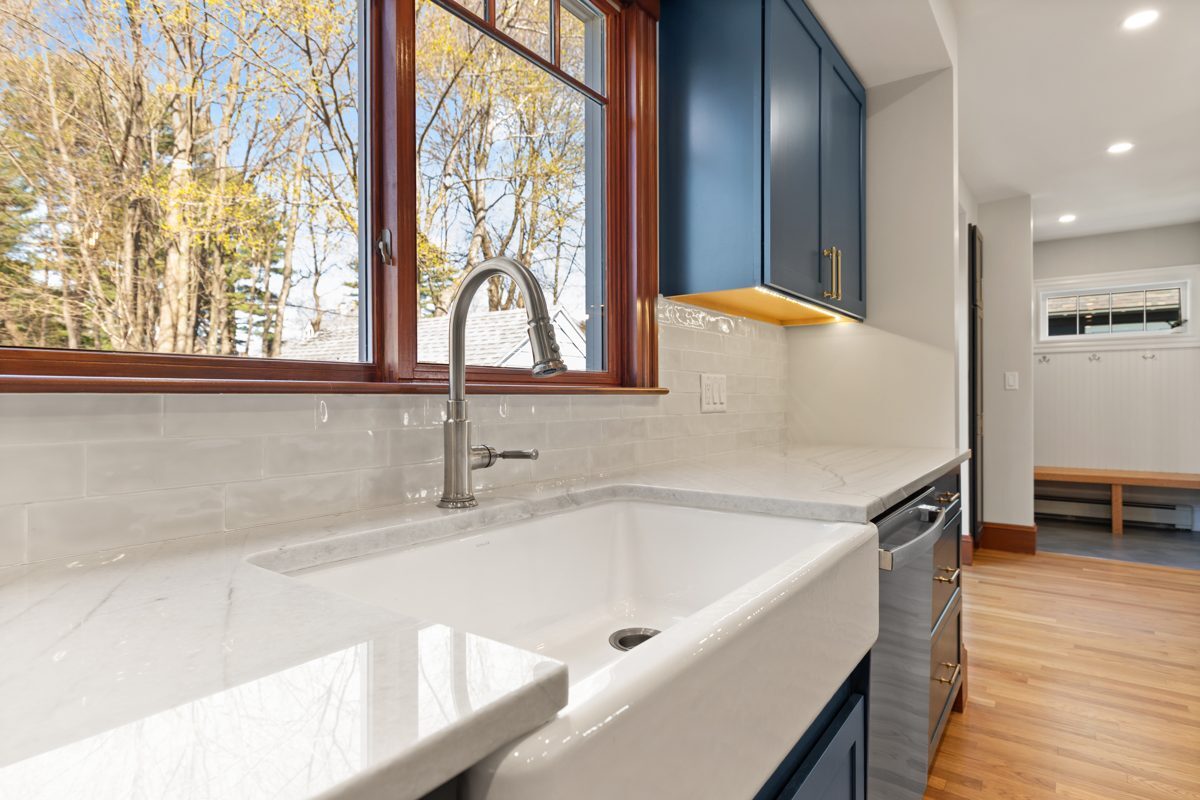 After: Kitchen: a tight corner sink under two small windows became a farmhouse sink under a wide window, with quartzite counters and a view through to the new mudroom.