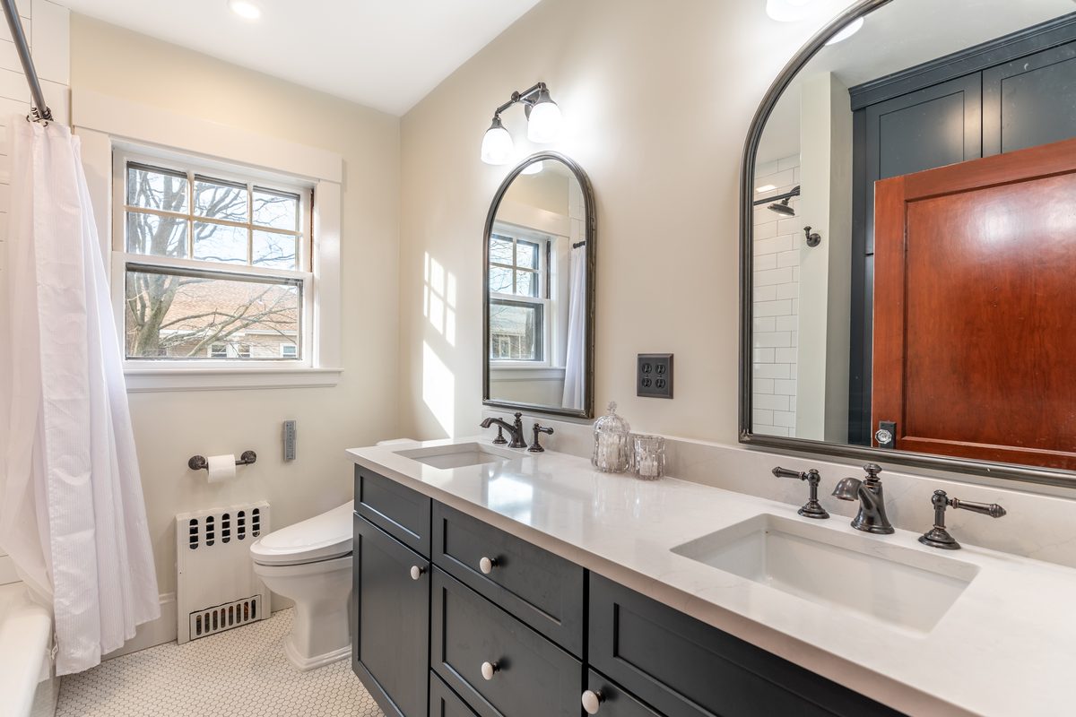 After: Upstairs bath: the single vanity and blue tile floor gave way to a double vanity, white hex tile and a radiator recessed into the wall under the window.