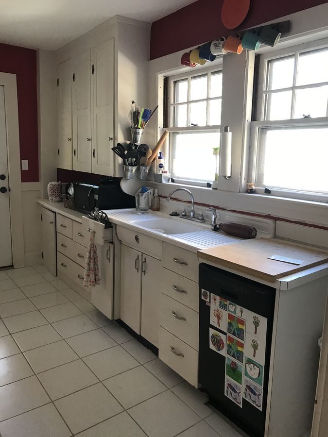 Before: Kitchen sink wall: the old drainboard sink and painted cabinets became a fireclay farmhouse sink, shaker cabinets and soapstone counters under the same twin windows.