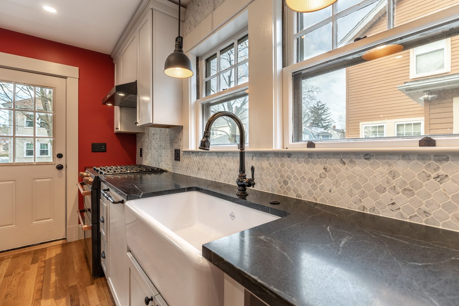 Farmhouse sink and black counters under double-hung windows in a remodeled Melrose, MA kitchen
