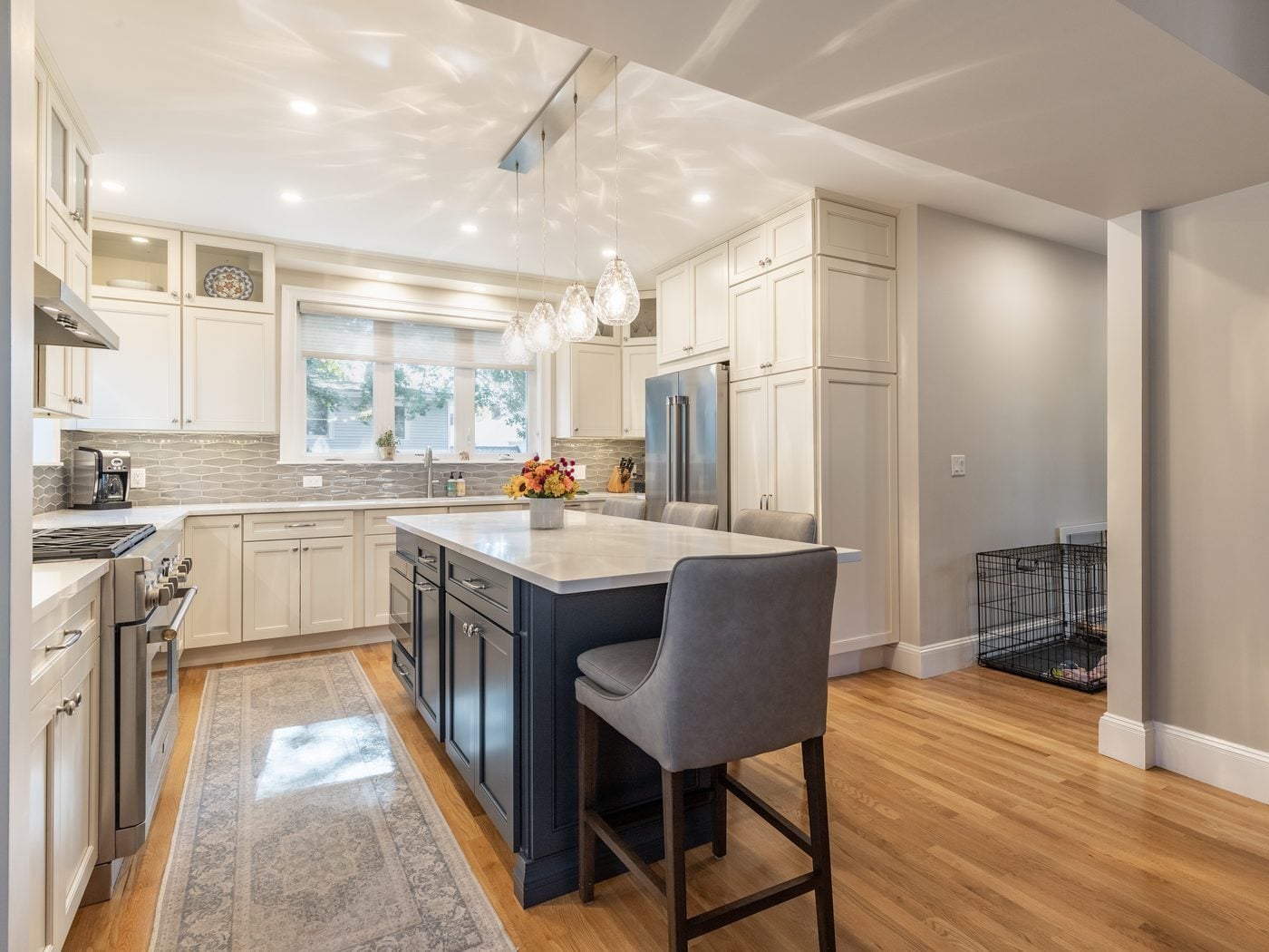 After: Kitchen: a cooktop island and a cramped corner were replaced by a navy island, a range wall with a hood, and glass-front uppers to the ceiling.